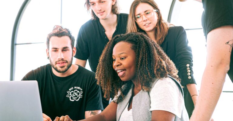 A diverse group of young professionals collaborating around a laptop in a modern office setting. Perfect for business or tech concepts.