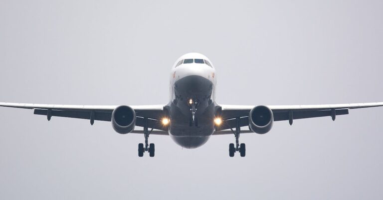 A commercial airliner captured head-on, preparing to land against a cloudy sky.
