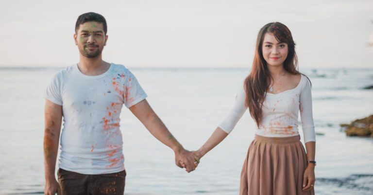 A cheerful couple holding hands by the sea, enjoying a playful day with paint splashes.