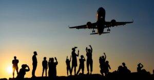 A dynamic silhouette of people photographing an airplane during a vibrant sunset.