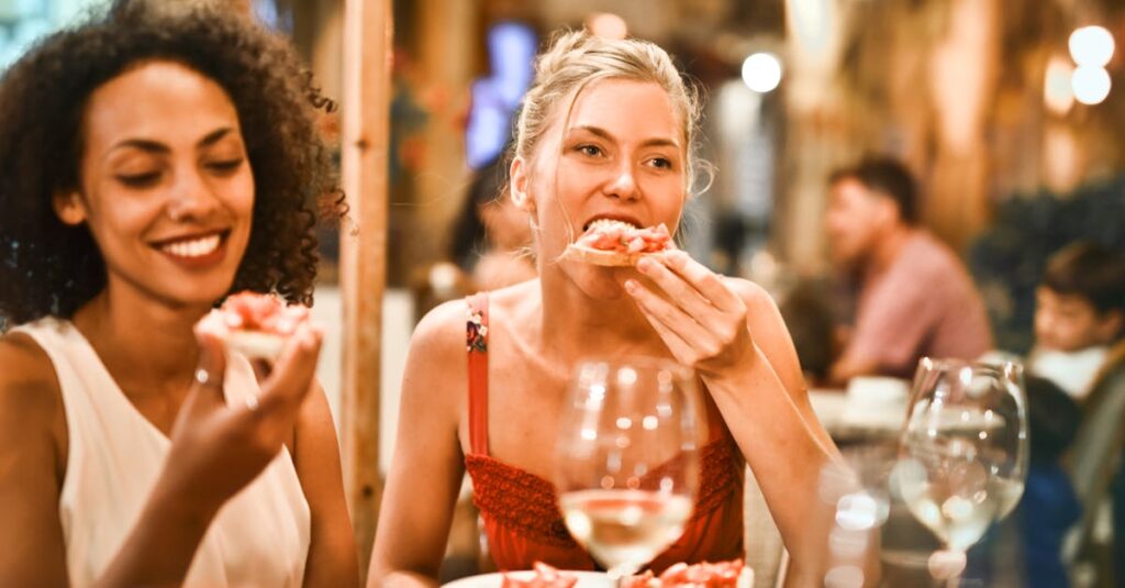 Two women enjoying bruschetta and wine at a vibrant outdoor restaurant.