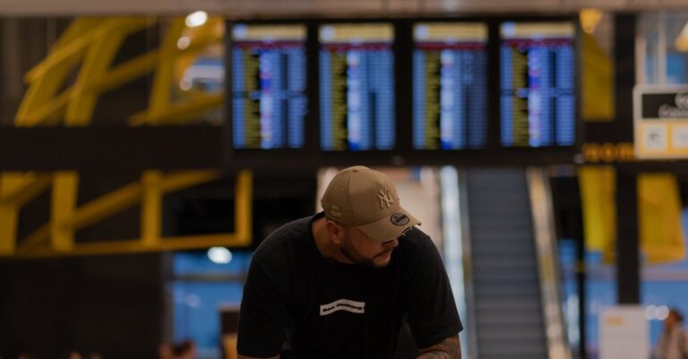 A man in casual attire sits with his backpack in an airport terminal, waiting for a flight.