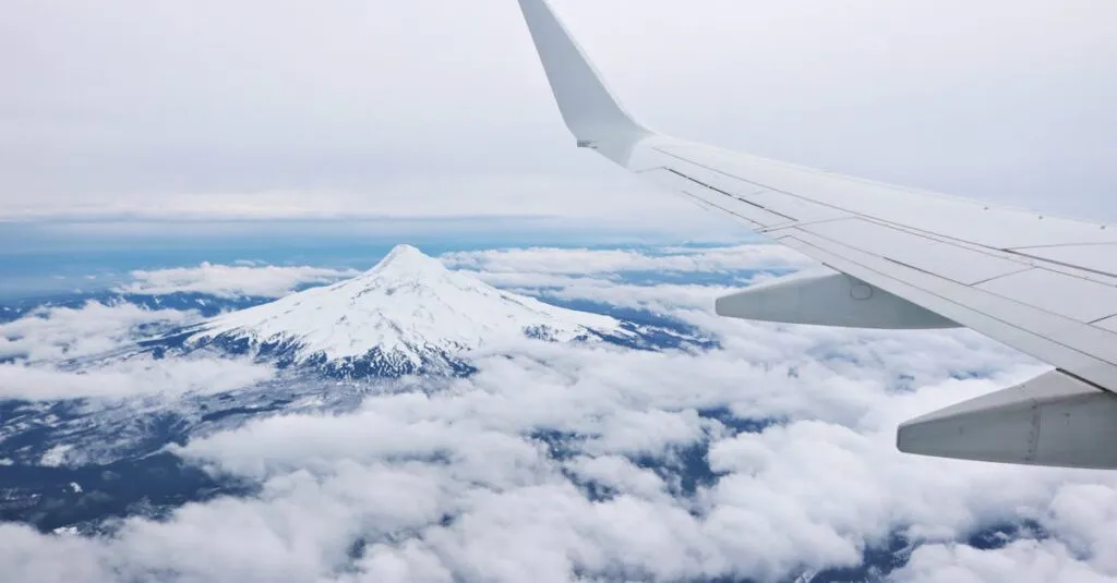 Mountain peak and airplane wing seen from above the clouds, showcasing a beautiful aerial view.