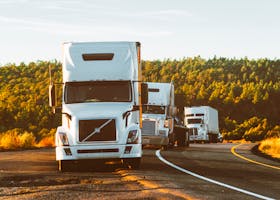 Three semi trucks driving on a highway through a forested landscape in Arizona.