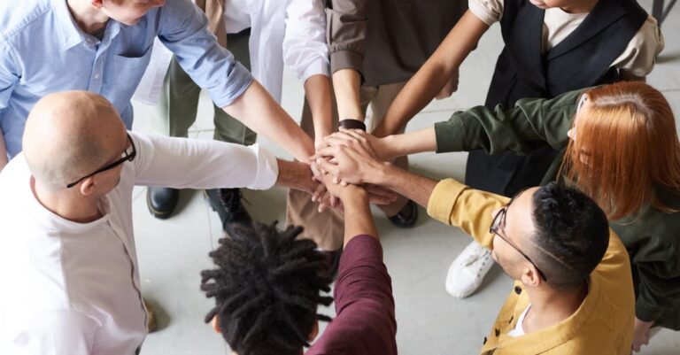 A diverse group of professionals joins hands in a team-building exercise indoors.