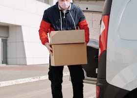 A delivery worker wearing a face mask unloading packages from a van in an urban area.