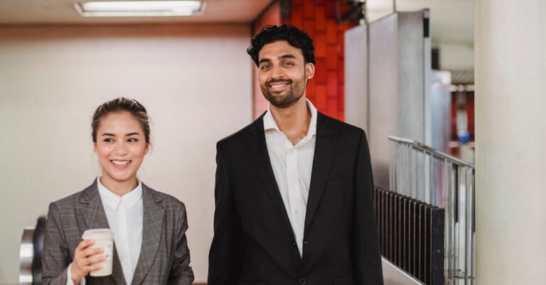 Two smiling professionals walking in a New York subway station, holding coffee and briefcase.