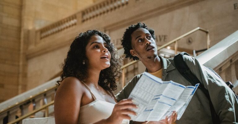 A young couple explores a railway station with a map, curiosity in their expressions.