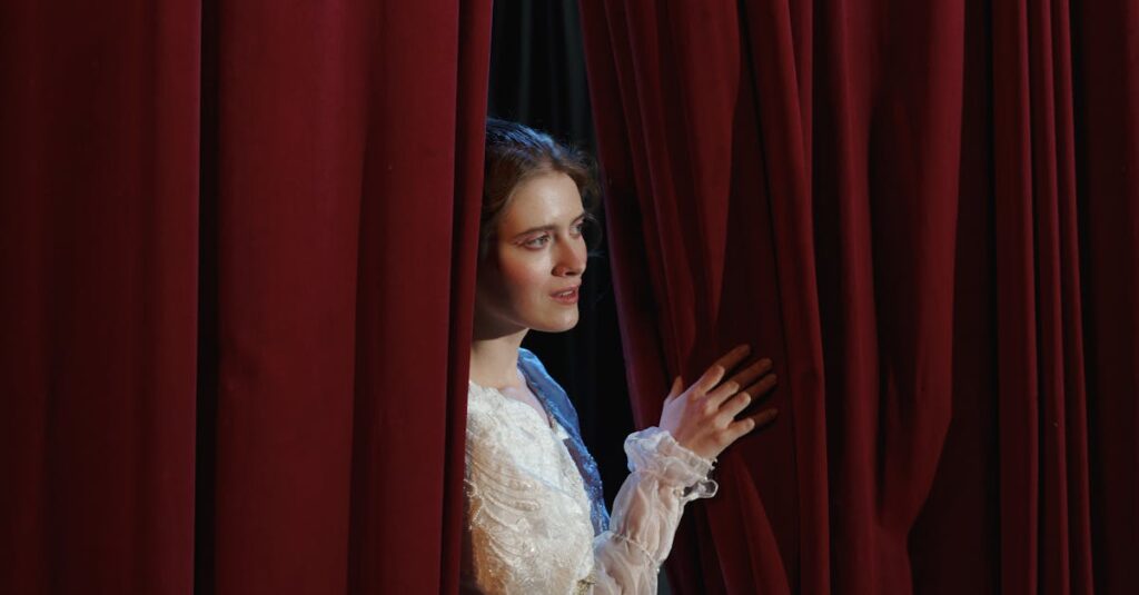 A woman in costume peeks through red theater curtains in a dramatic scene.