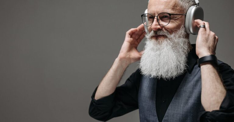 Mature man with white beard wearing wireless headphones and smiling in a studio setting.