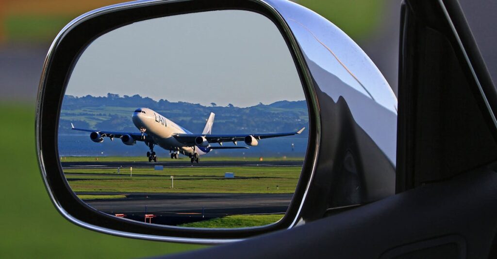 A jet airplane taking off is reflected in a car's side mirror, capturing a unique aviation perspective.