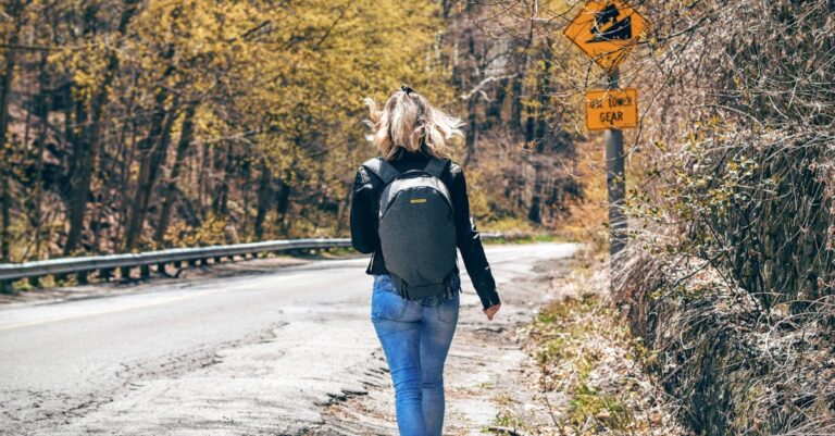 A woman with a backpack walks along a scenic forest road in spring, enjoying an outdoor hike.