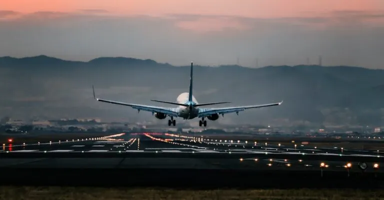 Dramatic view of a commercial airplane landing on a runway at sunset with mountains in the background.