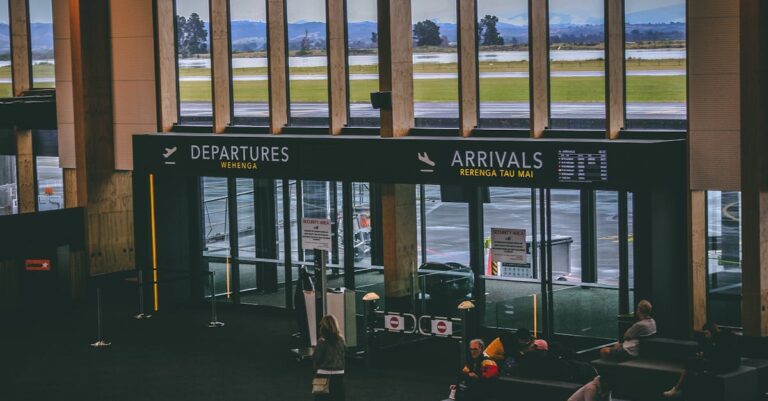 Busy airport terminal area with people, featuring departures and arrivals signs.