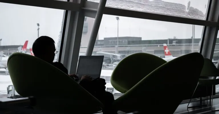 Silhouette of a man working on laptop at airport lounge with planes outside.