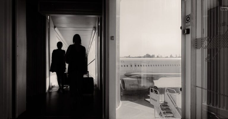 Silhouetted travelers walking through an airport jet bridge toward an airplane, conveying a travel mood.