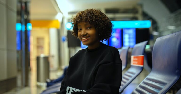 A young woman smiling while sitting at a train station, showcasing a joyful moment in travel.