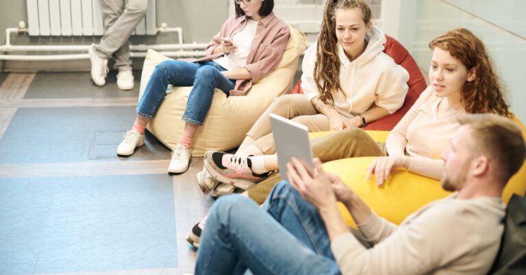 A group of young adults socializing indoors, sitting on bean bags, engaging with a tablet.