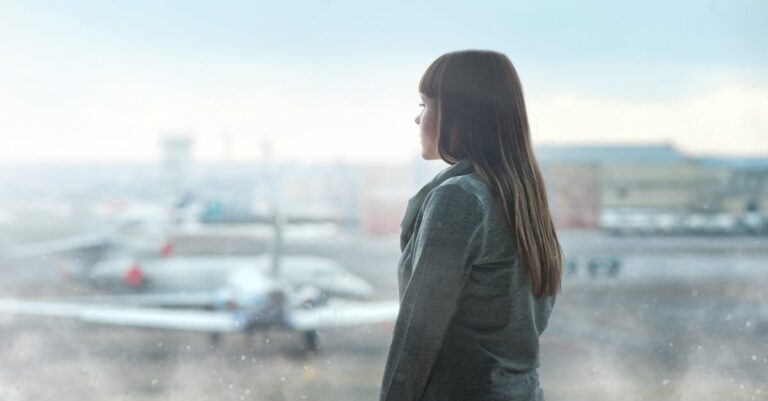 A woman gazing at airplanes through a window at Kyiv's airport terminal, capturing a moment of reflection.