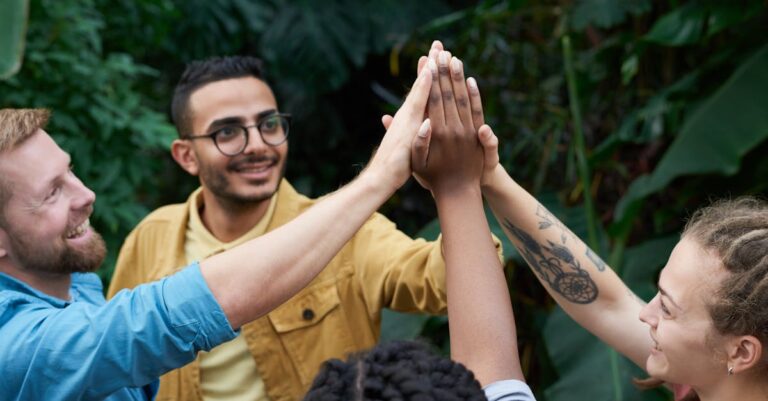 A joyful group of friends high-fiving outdoors, symbolizing teamwork and camaraderie.