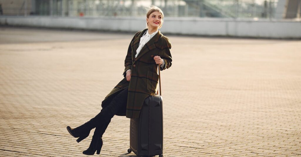 Smiling woman in a plaid coat sits on luggage at an airport terminal, enjoying a winter day.