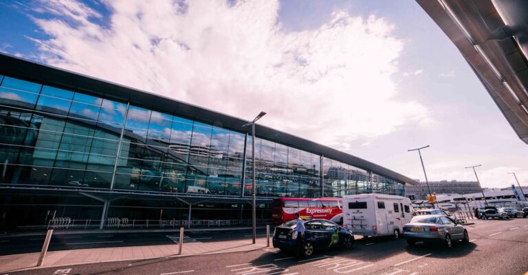 Daytime view of the modern terminal building at Dublin Airport, Ireland, with cars and buses parked outside.