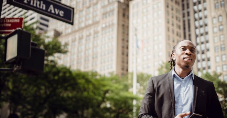 A young man stands on Fifth Avenue in New York City holding a smartphone, showcasing urban lifestyle.