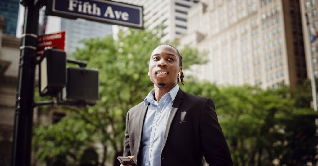 From below of young handsome black male in smart suit listening to music and waiting for car to pass while standing near street sign in Manhattan on sunny day