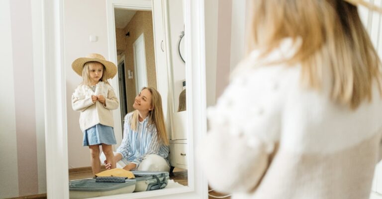 A mother and young daughter share a joyful moment dressing up indoors.