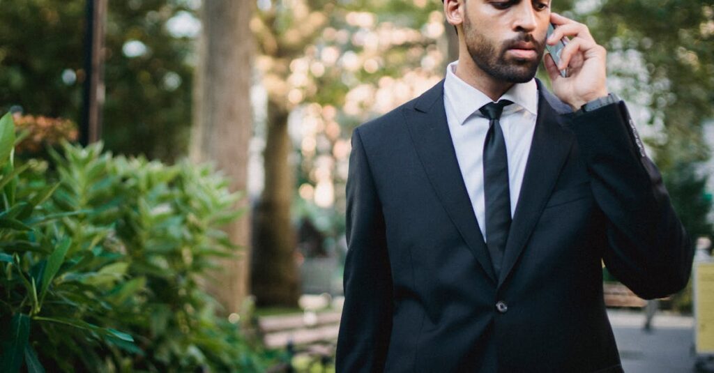 Confident businessman in black suit using smartphone outdoors in a park setting.