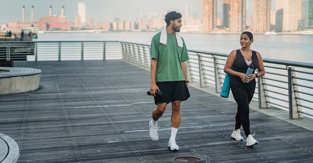 A man and woman in sportswear walking and exercising on a riverside boardwalk with a cityscape view.