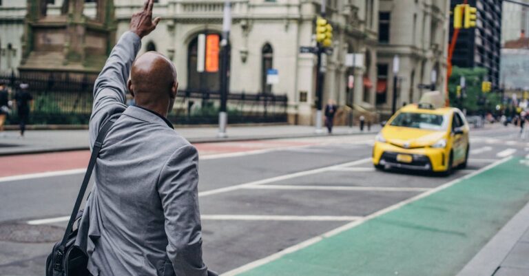 Back view of anonymous African American male with hand up catching yellow cab on blurred background of road