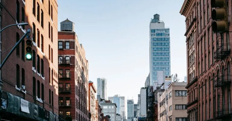 District of New York with aged residential buildings and modern commercial skyscrapers against cloudless blue sky
