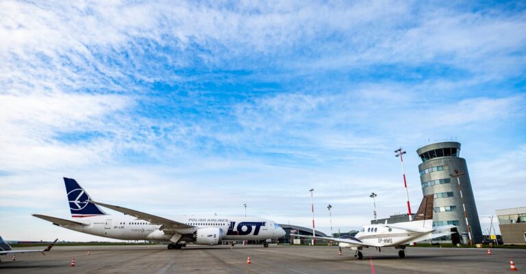 Polish Airlines plane on runway with control tower and jet under a blue sky.