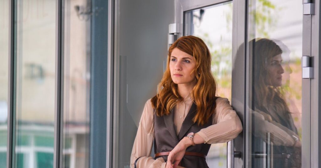 Stylish woman in urban environment standing by a glass door, reflecting thoughtful mood.