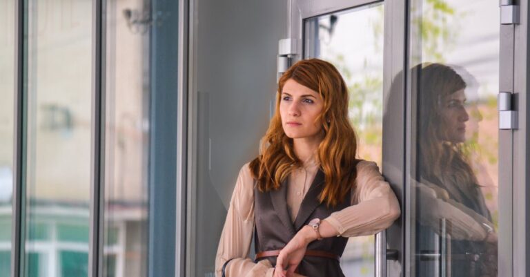 Stylish woman in urban environment standing by a glass door, reflecting thoughtful mood.