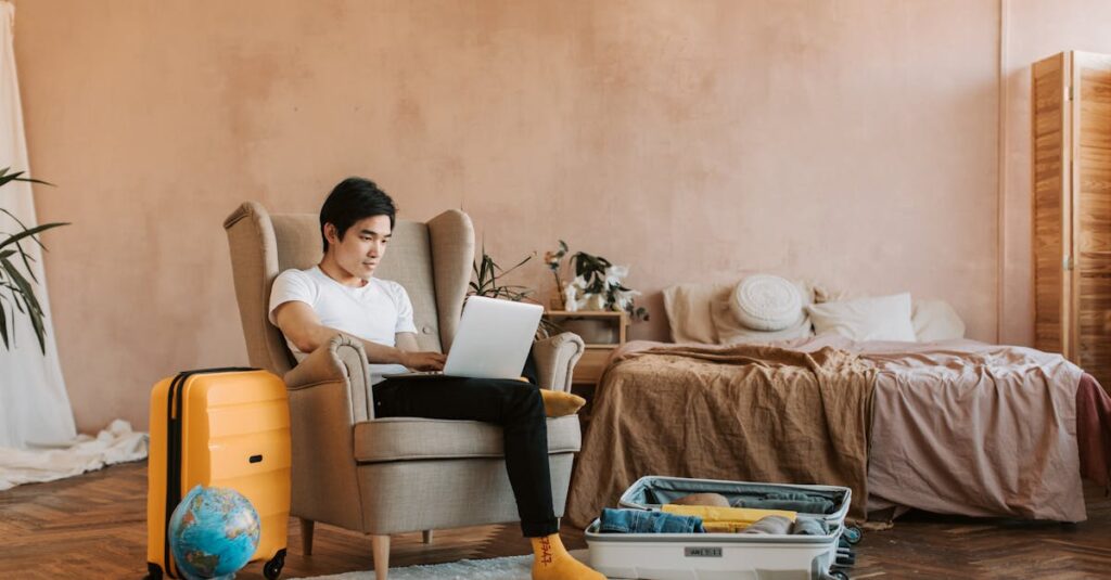 A man uses a laptop while packing a suitcase at home, ready for travel.