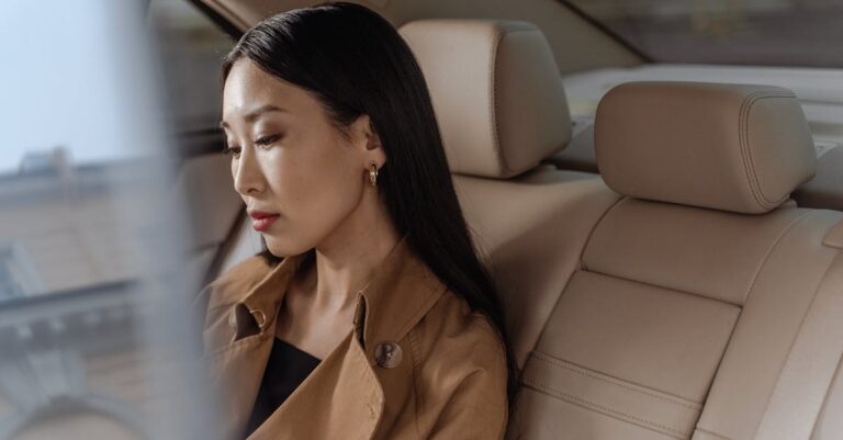 An elegant Asian woman sits thoughtfully in a luxurious car interior.