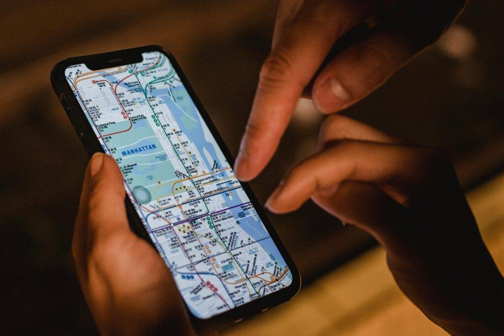 Close-up of hands using a smartphone with a New York City subway map at night, highlighting modern navigation.