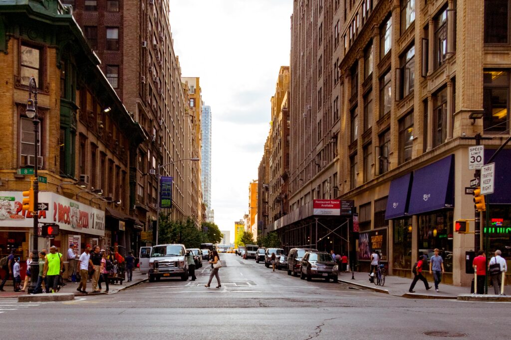 Lively urban street in New York City with pedestrians and vehicles on a sunny day.