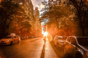 Silhouette of a cyclist during sunset on a New York City street with urban buildings and cars.