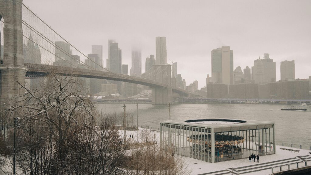 Winter view of Brooklyn Bridge and Manhattan skyline with snow-covered Jane's Carousel.