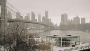 Winter view of Brooklyn Bridge and Manhattan skyline with snow-covered Jane's Carousel.