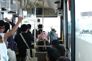 Passengers on a bus ride, holding onto rails and carrying backpacks, showcasing urban transportation.