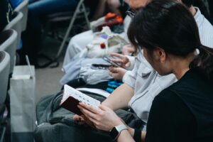 Close-up of people sitting in a crowd, reading a book and checking a smartphone.