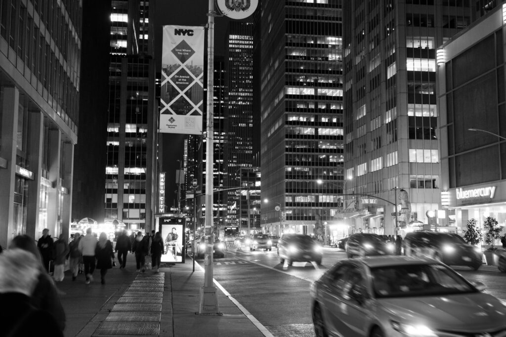 Black and white photo capturing busy night traffic and pedestrians in downtown New York City.
