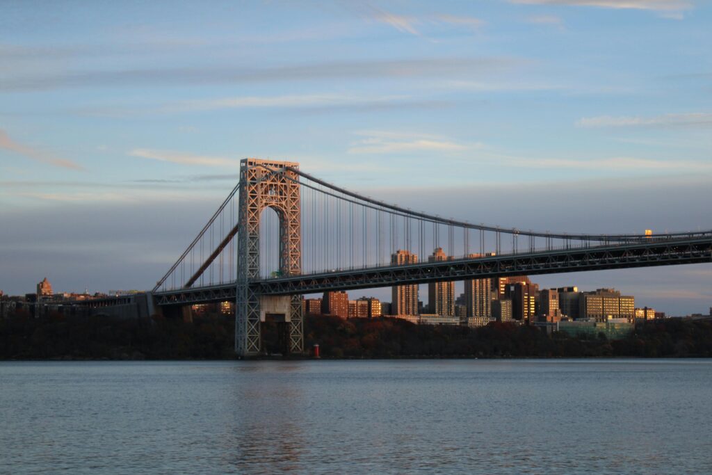 Scenic view of the George Washington Bridge and NYC skyline at sunset over Hudson River.