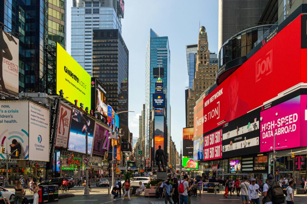 Bustling Times Square NYC with vibrant billboards and lively crowd under a bright sky.
