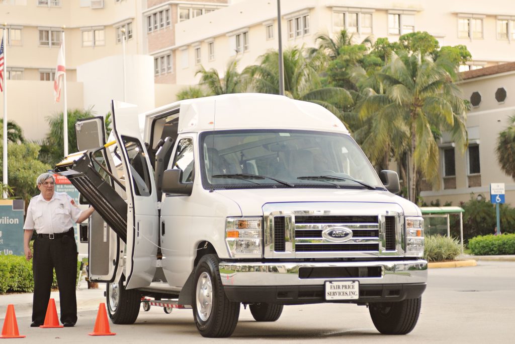 White passenger van with a deployed lift, parked near modern urban buildings.