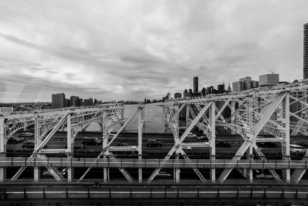 Black and white photo of New York City bridge with skyline in the background.